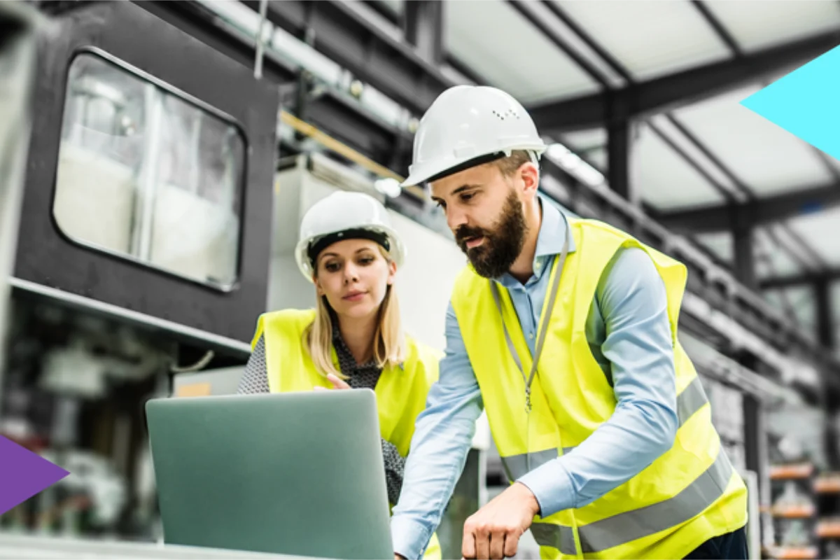 Man and woman operating hardware in factory wearing hi vis jackets and hardhats